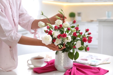 Woman with bouquet of fresh flowers in stylish vase at table, closeup