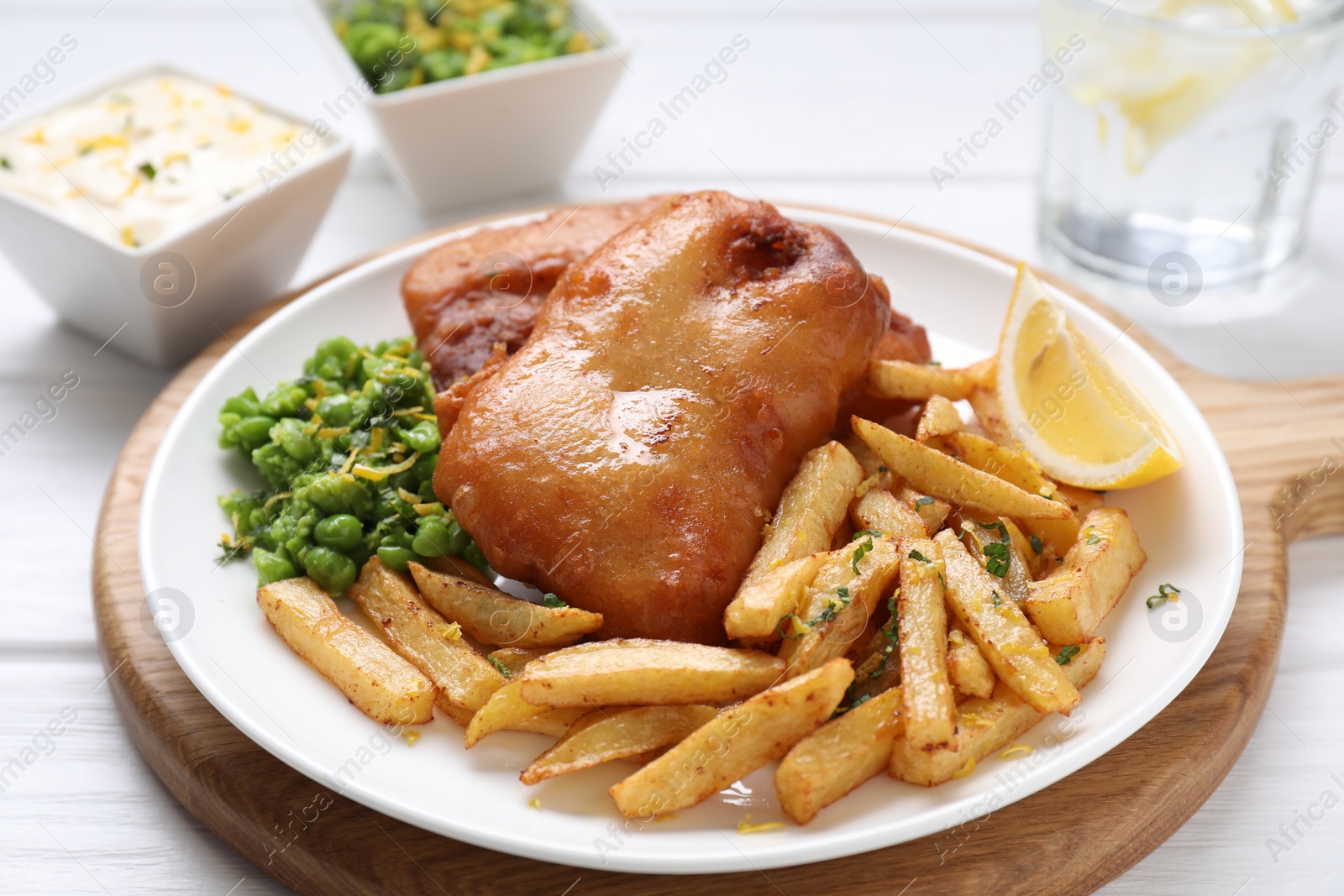 Photo of Tasty fish, chips, sauce, peas and lemon on white wooden table, closeup