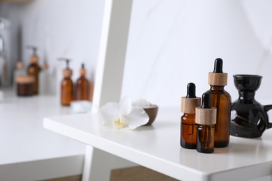 Bottles of essential oil on white shelf in bathroom. Space for text