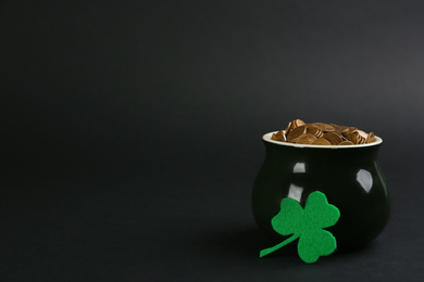 Photo of Pot of gold coins and clover on black background, space for text. St. Patrick's Day celebration