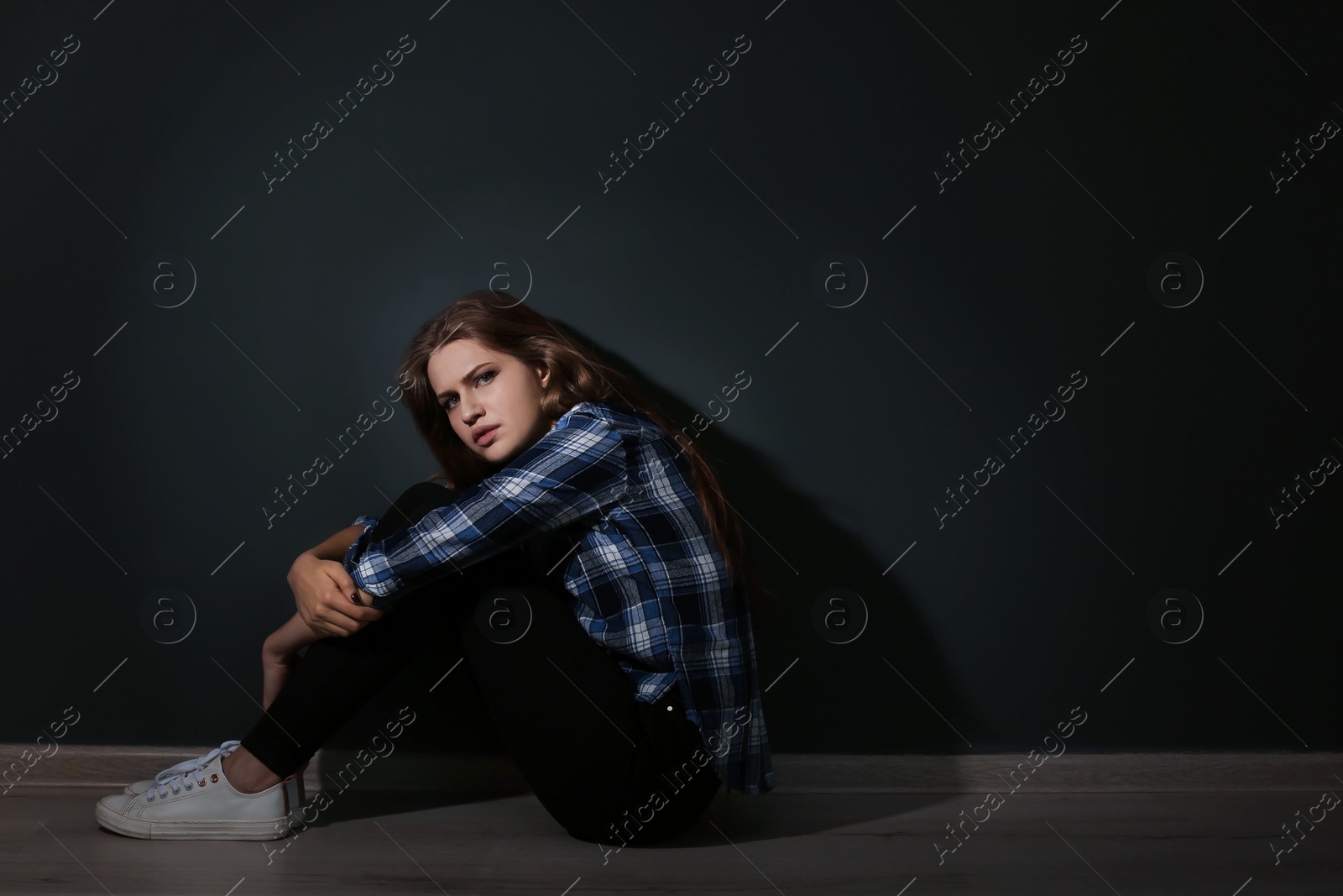 Photo of Depressed young woman sitting on floor in darkness