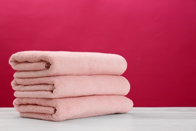 Stack of soft clean towels on table against color background. Space for text