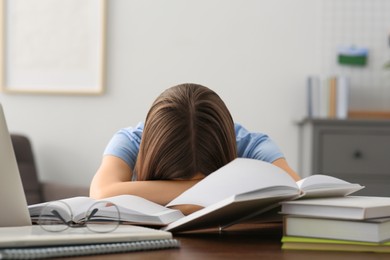 Photo of Young tired woman sleeping near books at wooden table indoors