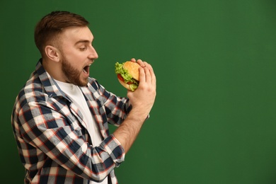Photo of Young man eating tasty burger on color background. Space for text