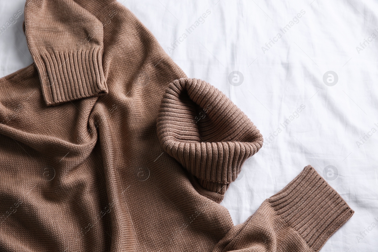 Photo of Brown warm sweater on white crumpled fabric, top view