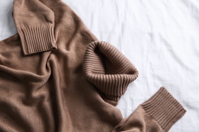 Photo of Brown warm sweater on white crumpled fabric, top view