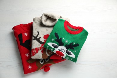 Photo of Folded warm Christmas sweaters on white wooden table, top view