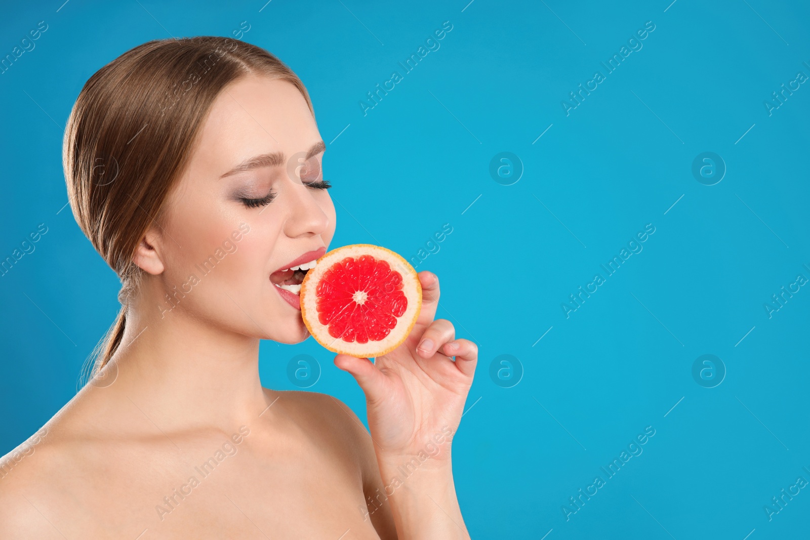 Photo of Young woman with cut grapefruit on blue background, space for text. Vitamin rich food