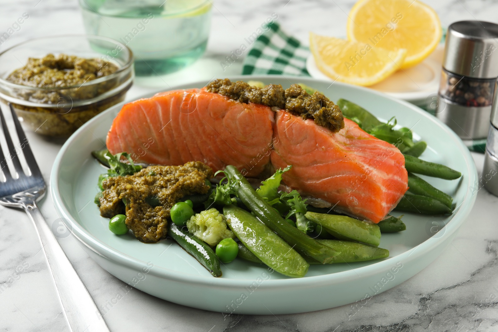 Photo of Tasty cooked salmon with pesto sauce and fresh salad served on white marble table