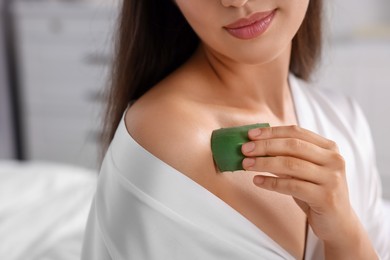 Photo of Young woman applying aloe gel from leaf onto her shoulder indoors, closeup