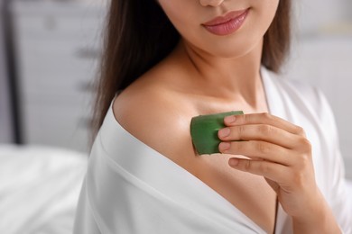 Young woman applying aloe gel from leaf onto her shoulder indoors, closeup