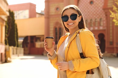 Happy young woman with coffee on city street in morning