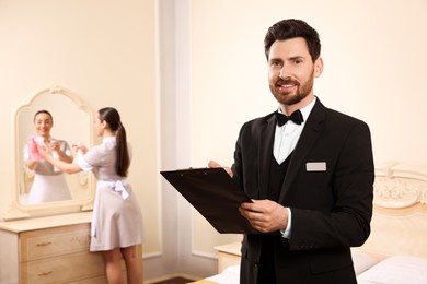 Photo of Man wearing suit with clipboard checking maid's work in hotel room, space for text. Professional butler courses