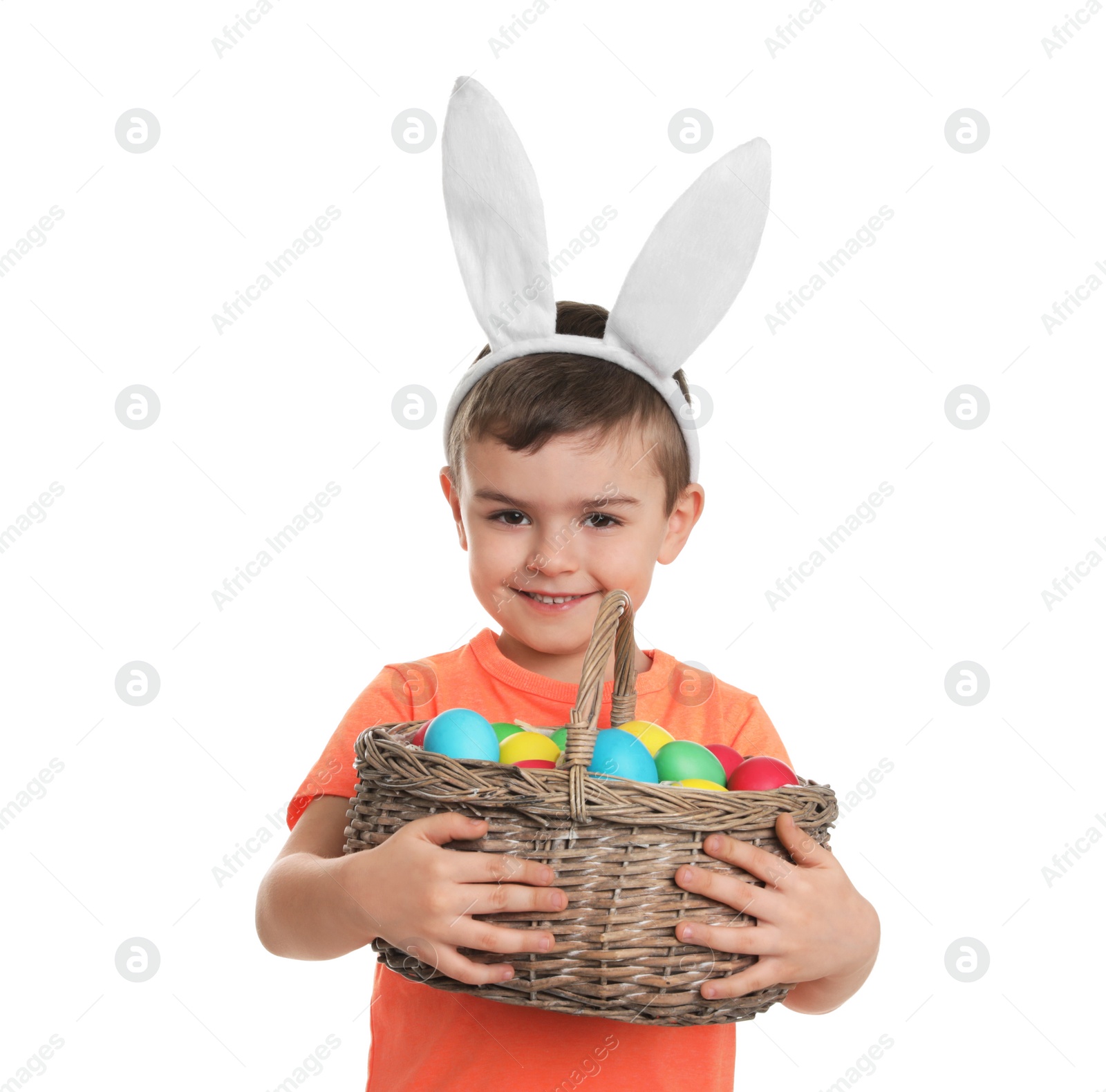 Photo of Little boy in bunny ears headband holding basket with Easter eggs on white background