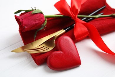 Photo of Closeup view of cutlery with napkin and decorative heart on white wooden table. Valentine's Day romantic dinner