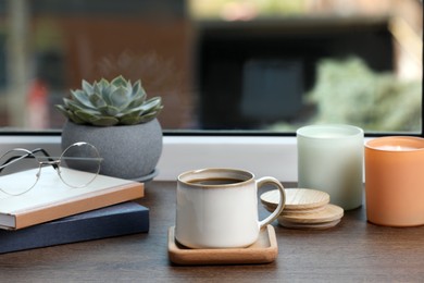 Photo of Cup of coffee with books and home decor on wooden window sill