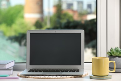 Cup of tea, laptop with blank screen, books and succulent on wooden window sill. Space for text