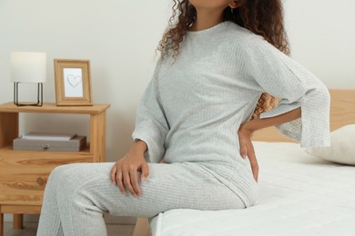 Photo of Woman suffering from back pain after sleeping on uncomfortable mattress at home, closeup