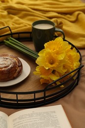 Bouquet of beautiful daffodils, bun and coffee on bed