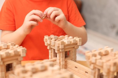 Little boy playing with wooden construction set at table in room, closeup. Child's toy