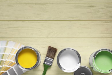 Photo of Cans of paints, palette and brush on yellow wooden table, flat lay. Space for text