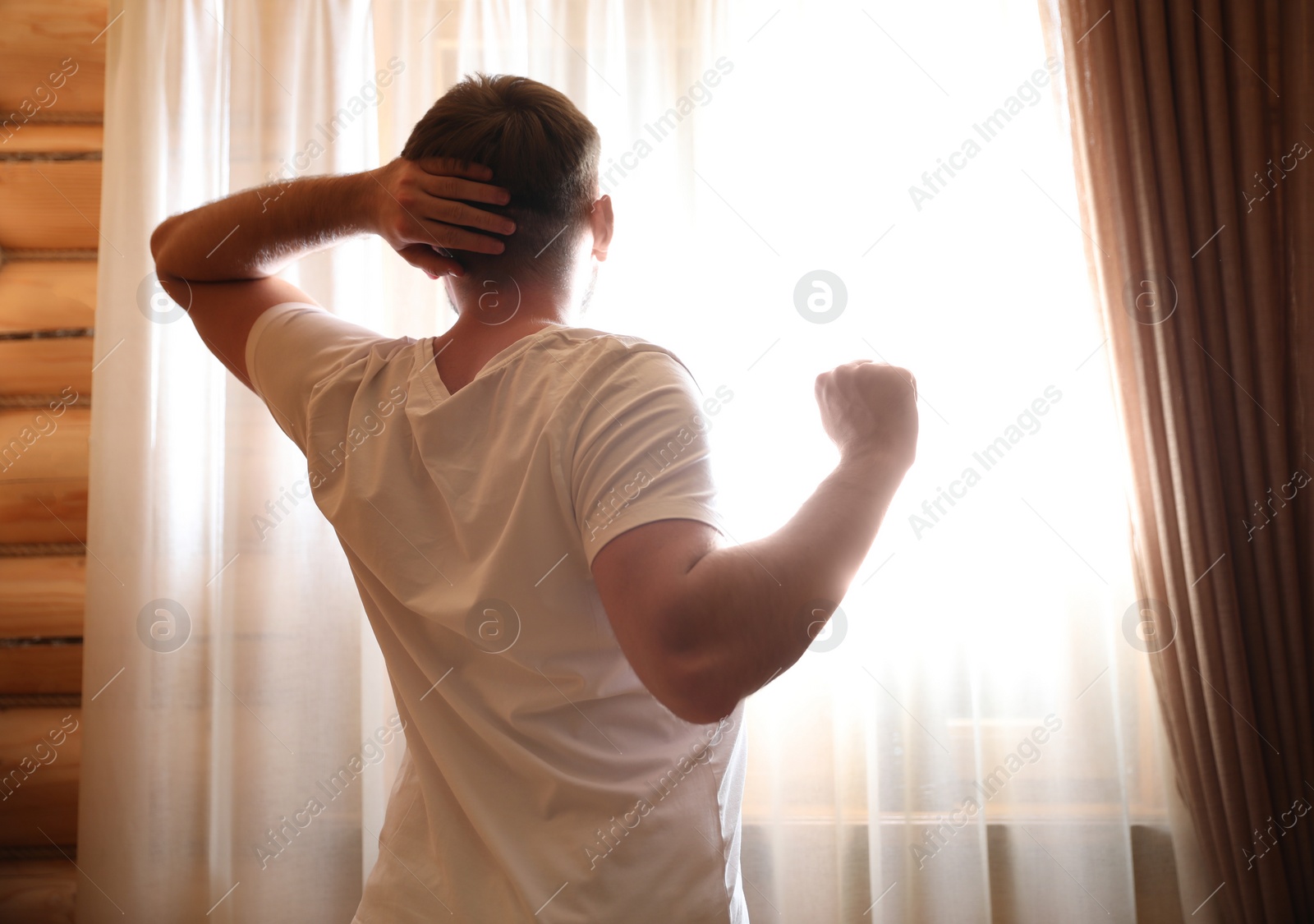 Photo of Man stretching near window indoors. Lazy morning