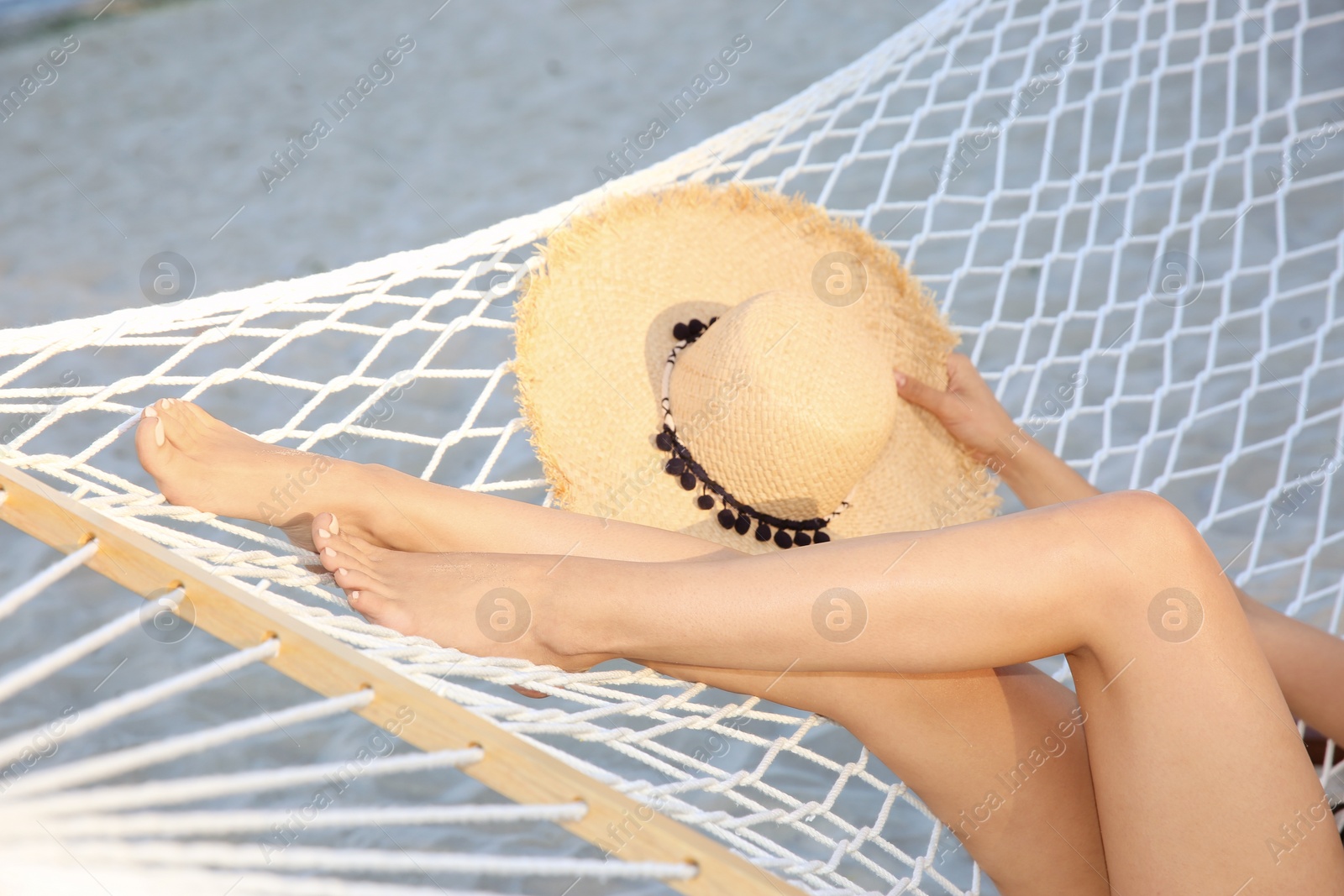 Photo of Young woman with straw hat resting in hammock at seaside. Summer vacation