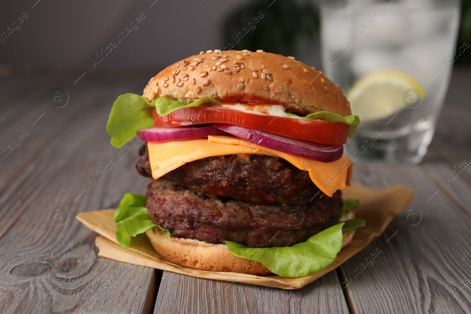 Photo of Tasty cheeseburger with patties and tomato on wooden table, closeup