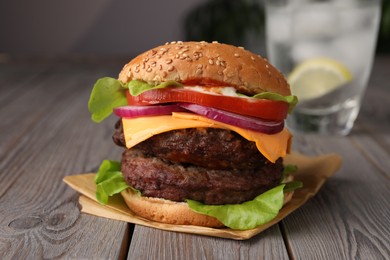 Photo of Tasty cheeseburger with patties and tomato on wooden table, closeup