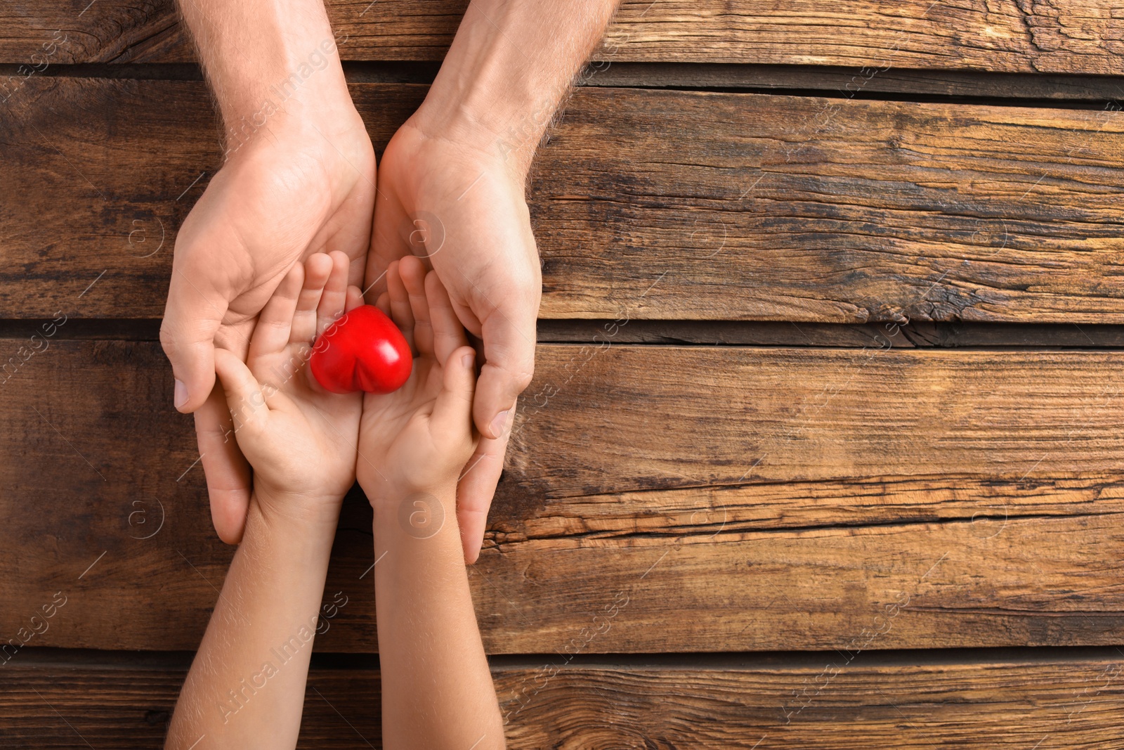 Photo of Family holding small red heart in hands on wooden background