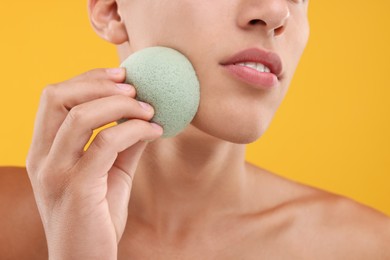 Photo of Young man washing his face with sponge on orange background, closeup