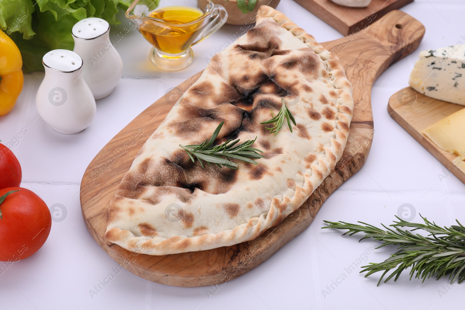 Photo of Tasty pizza calzone with rosemary and different products on white tiled table