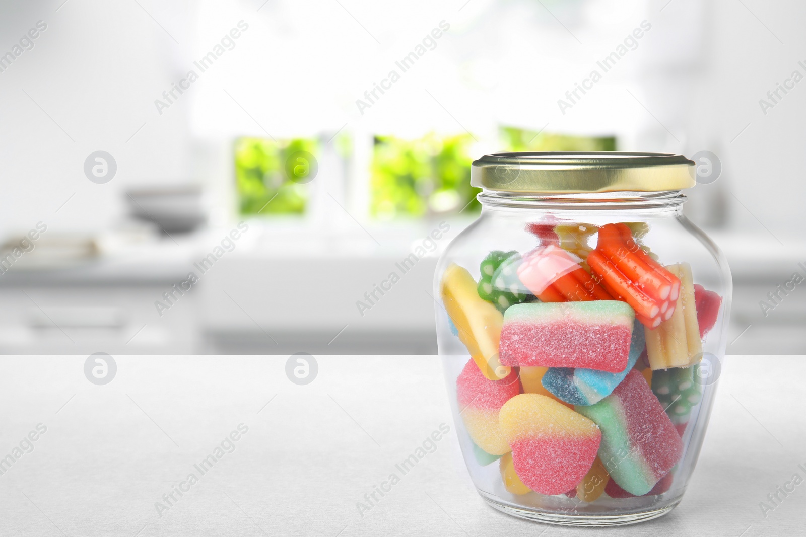 Image of Glass jar with tasty gummy candies on white table in kitchen. Space for text