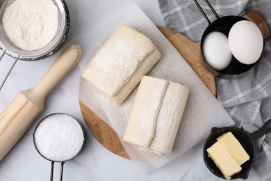 Photo of Raw puff pastry dough and ingredients on white marble table, flat lay