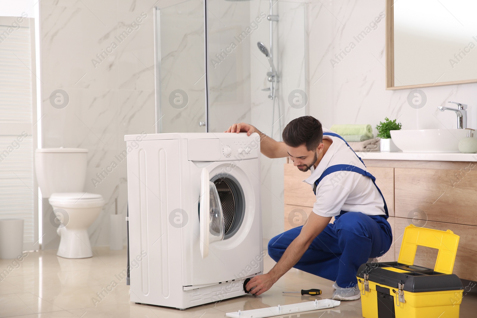 Photo of Professional plumber repairing washing machine in bathroom