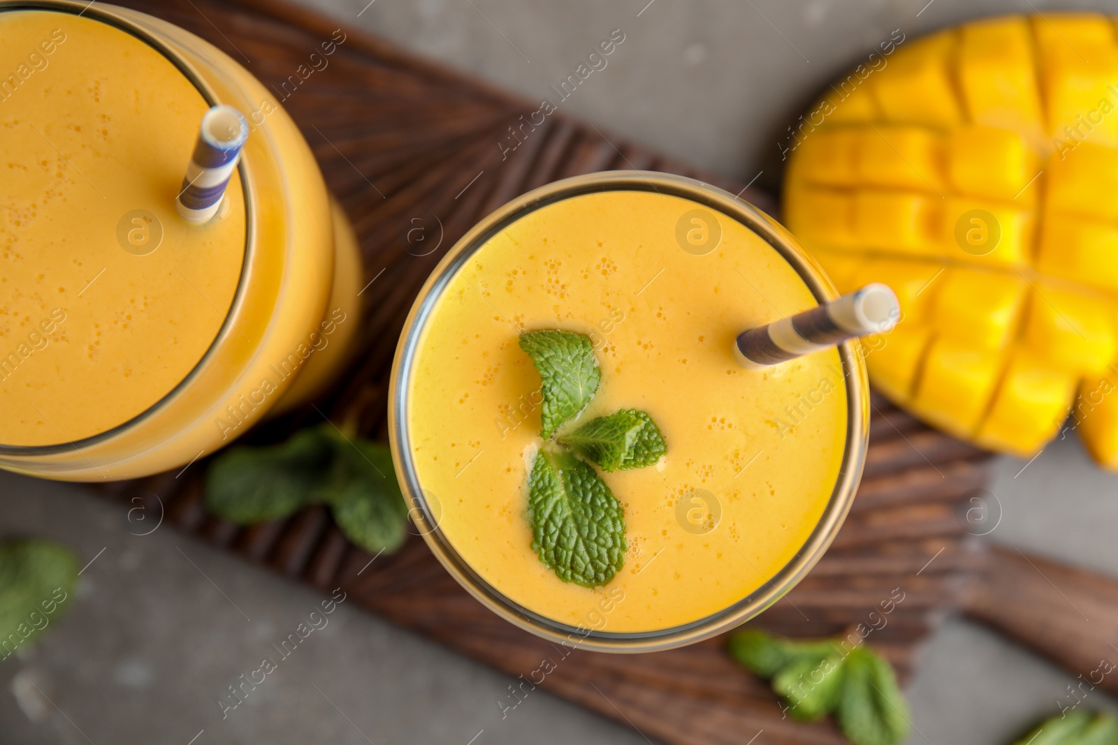 Photo of Glasses of fresh mango drink and fruit on board, top view