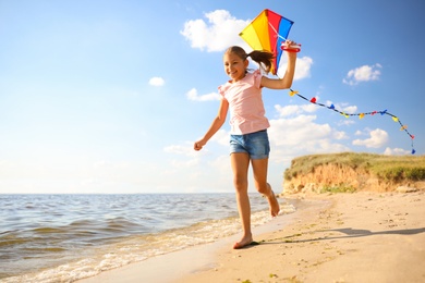 Photo of Cute little child with kite running on beach near sea. Spending time in nature