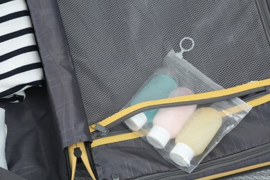 Photo of Plastic bag of cosmetic travel kit and clothes in suitcase, top view. Bath accessories