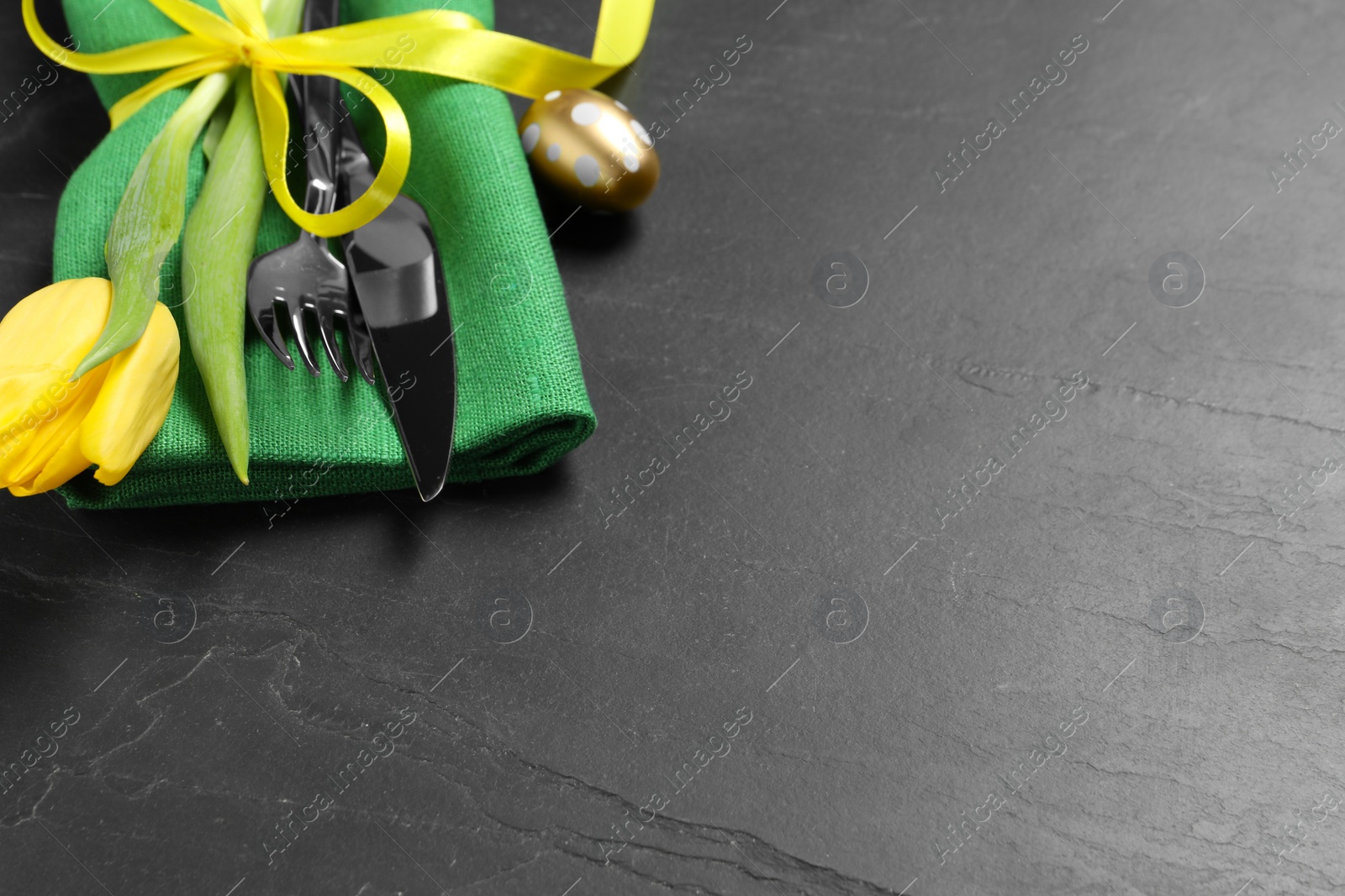 Photo of Cutlery set, painted egg and beautiful flower on black table, closeup with space for text. Easter celebration