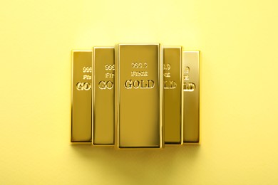 Photo of Stack of shiny gold bars on yellow background, top view