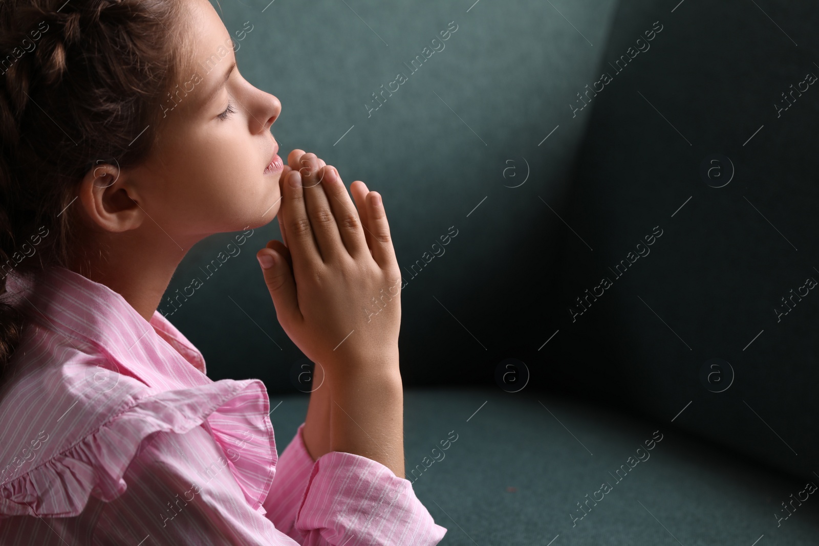 Photo of Cute little girl with hands clasped together praying. Space for text