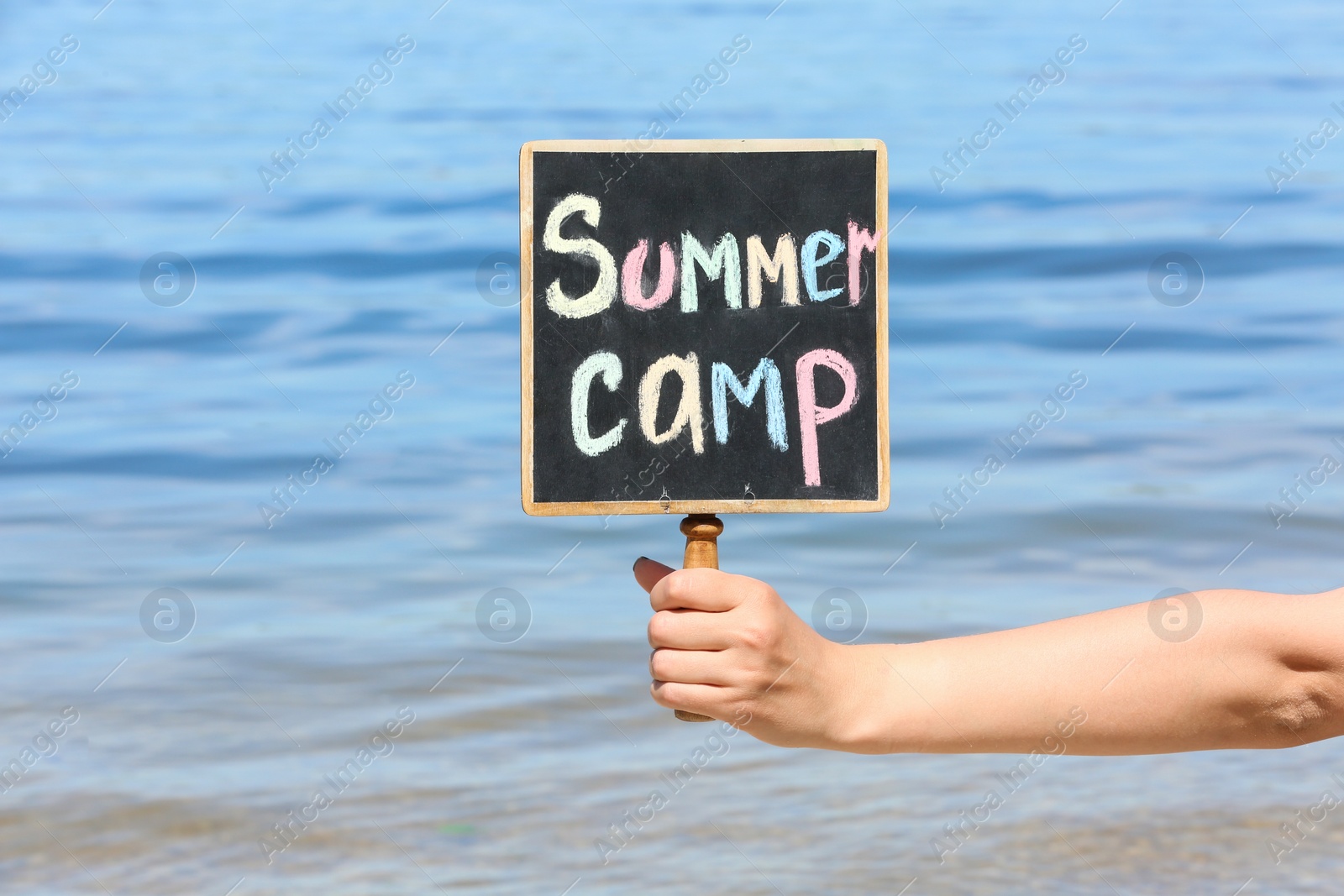 Photo of Woman holding little blackboard with text SUMMER CAMP near sea