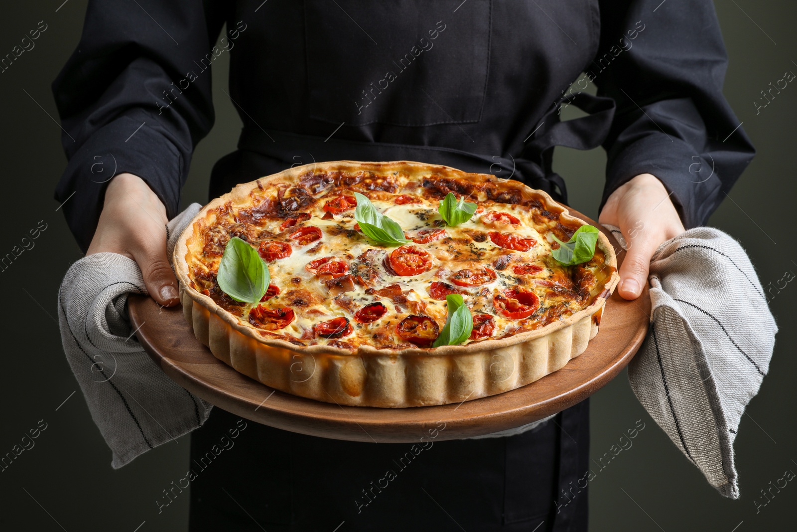 Photo of Woman holding delicious homemade quiche with prosciutto on dark background, closeup