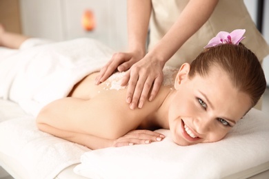 Beautiful young woman having massage with body scrub in spa salon