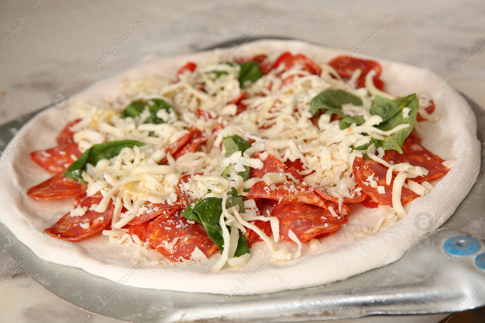 Photo of Peel with raw traditional Italian pizza on table in restaurant kitchen, closeup