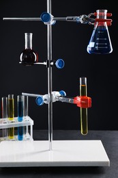 Photo of Retort stand and laboratory glassware with liquids on table against black background