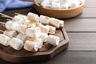 Sticks with roasted marshmallows on wooden table, closeup