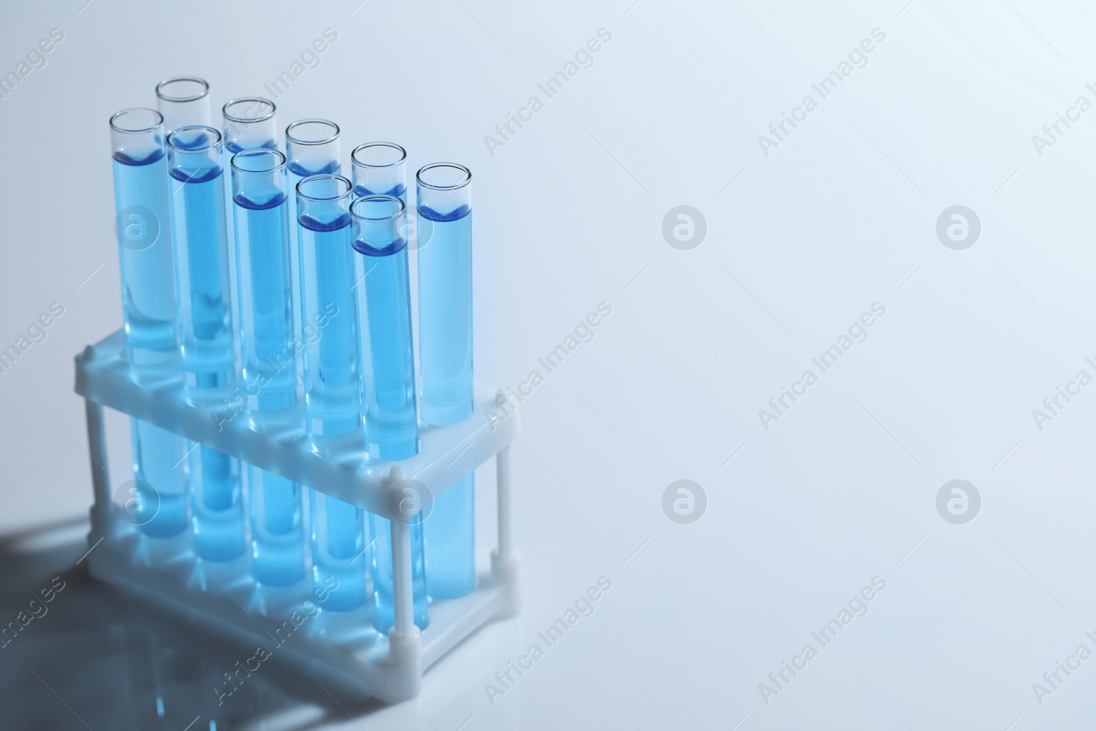 Photo of Test tubes with blue liquid on light background. Space for text
