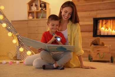 Mother and son with flashlight reading book at home
