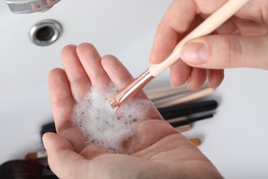 Photo of Woman washing makeup brush with soap, closeup